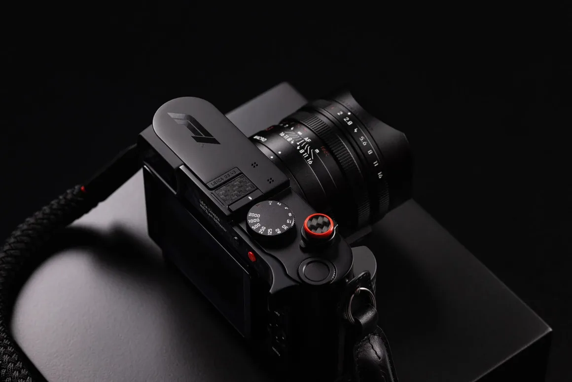 Leica Q3 43 Formula 1 Edition: Karbon Fiber Detaylı Özel Seri 20 Üst plakasında F1 logosu bulunan siyah Leica fotoğraf makinesi koyu bir yüzeyde duruyor; objektif üzerinde diyafram ve mesafe işaretleri görülüyor.