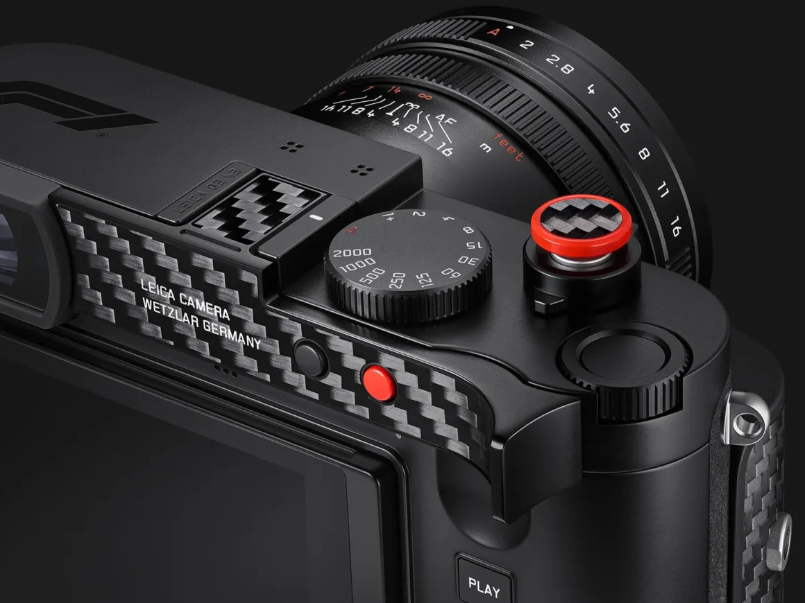 Leica Q3 43 Formula 1 Edition: Karbon Fiber Detaylı Özel Seri 25 Karbon fiber detaylı siyah fotoğraf makinesinin yakın plan görünümünde enstantane kadranı, kırmızı deklanşör düğmesi ve diyafram işaretli objektif görülüyor.