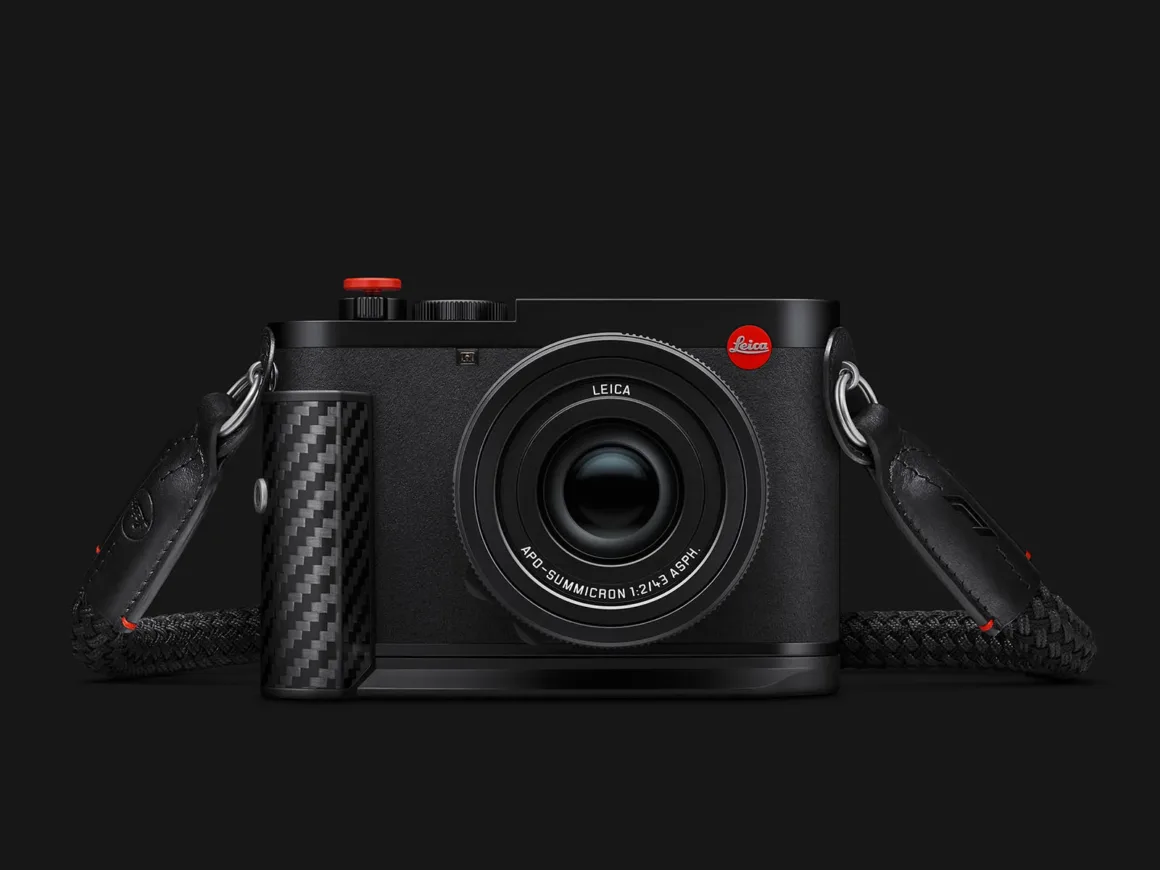 Leica Q3 43 Formula 1 Edition: Karbon Fiber Detaylı Özel Seri 26 Karbon fiber tutma bölümüne, kırmızı deklanşör düğmesine ve siyah örgülü askıya sahip Leica fotoğraf makinesi koyu fonda gösteriliyor.