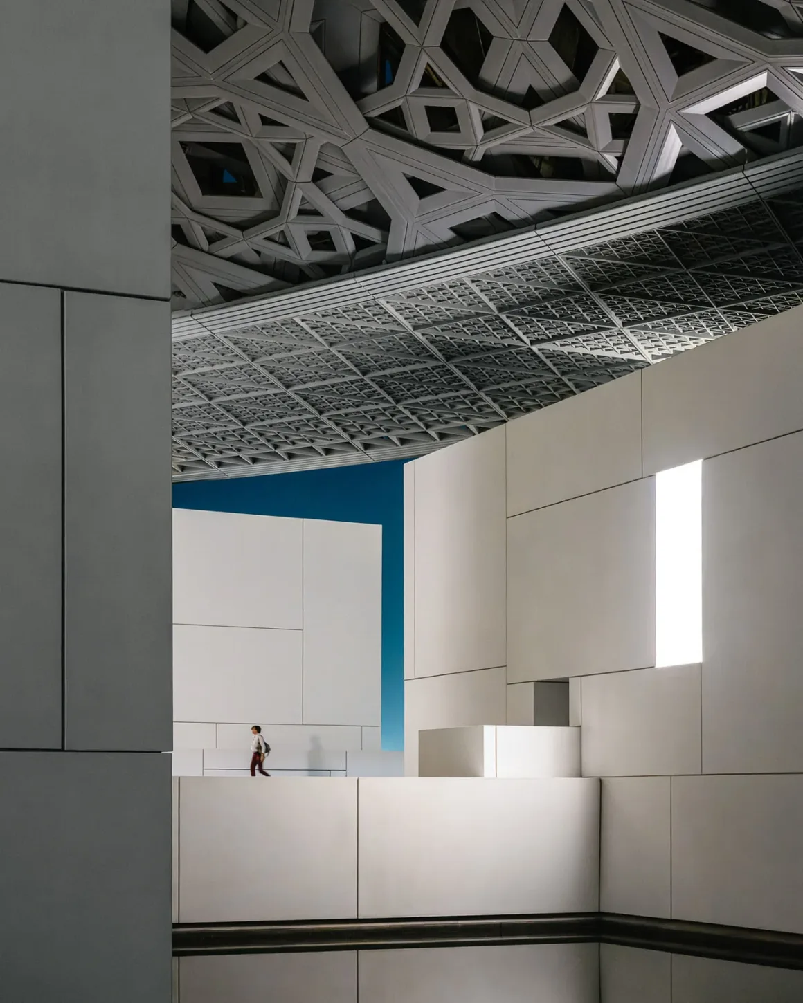 Architecture Photography MasterPrize 2026 Kazananları Açıklandı 34 Bir kişi Louvre Abu Dhabi’de büyük ve karmaşık geometrik kubbe yapısının altındaki beyaz yürüyüş yolunda ilerliyor.