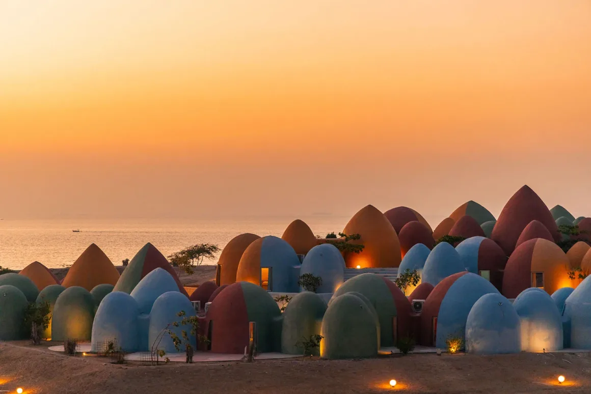 Architecture Photography MasterPrize 2026 Kazananları Açıklandı 26 Gün batımında sahil boyunca sıralanan renkli, kubbe biçimli yapılardan oluşan bir kompleks ve arka planda deniz görülüyor.