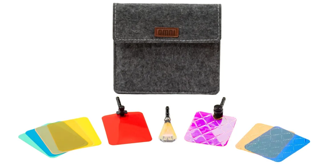 Lensbaby Omni Color II ve Omni Crystal II ile Çekim Sırasında Yaratıcı Efektler 19 Üzerinde omni logosu bulunan gri keçe taşıma çantasının önünde çeşitli renkli fotoğraf filtreleri, iki klips ve kristal prizma yer alıyor.