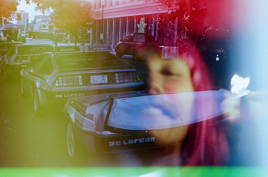 Psychedelic Blues: Analog Fotoğrafçılıkta Renk, Işık ve Rastlantının Peşinde 19 Şehir caddesinde park edilmiş iki gümüş renkli DeLorean otomobilinin üzerinde bir insan yüzünün çoklu pozlama etkisiyle belirdiği deneysel analog fotoğraf.
