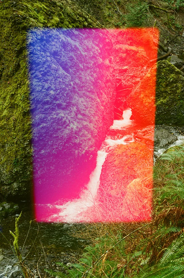 Psychedelic Blues: Analog Fotoğrafçılıkta Renk, Işık ve Rastlantının Peşinde 29 Yosunlu kaya yüzeylerinin arasında akan küçük bir şelale. Görüntünün üzerinde mavi, pembe ve turuncu tonlardan oluşan dikey bir ışık geçişi bulunuyor.