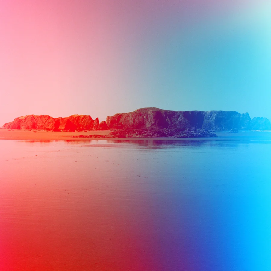 Psychedelic Blues: Analog Fotoğrafçılıkta Renk, Işık ve Rastlantının Peşinde 32 Pembe ve mavi tonlara dönüşen gökyüzünün altında, sakin ve yansıtıcı bir sahilin ortasında duran kayalık ada.