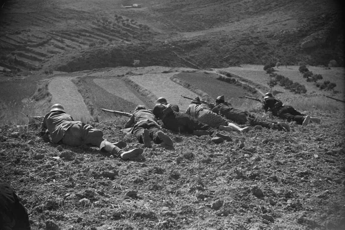 Robert Capa’nın Death in the Making Kitabı 88 Yıl Sonra Yeniden Basılıyor 19 Miğferli beş asker toprak bir yamaca yüzüstü uzanmış, tüfeklerini aşağıdaki vadiye doğru doğrultuyor.