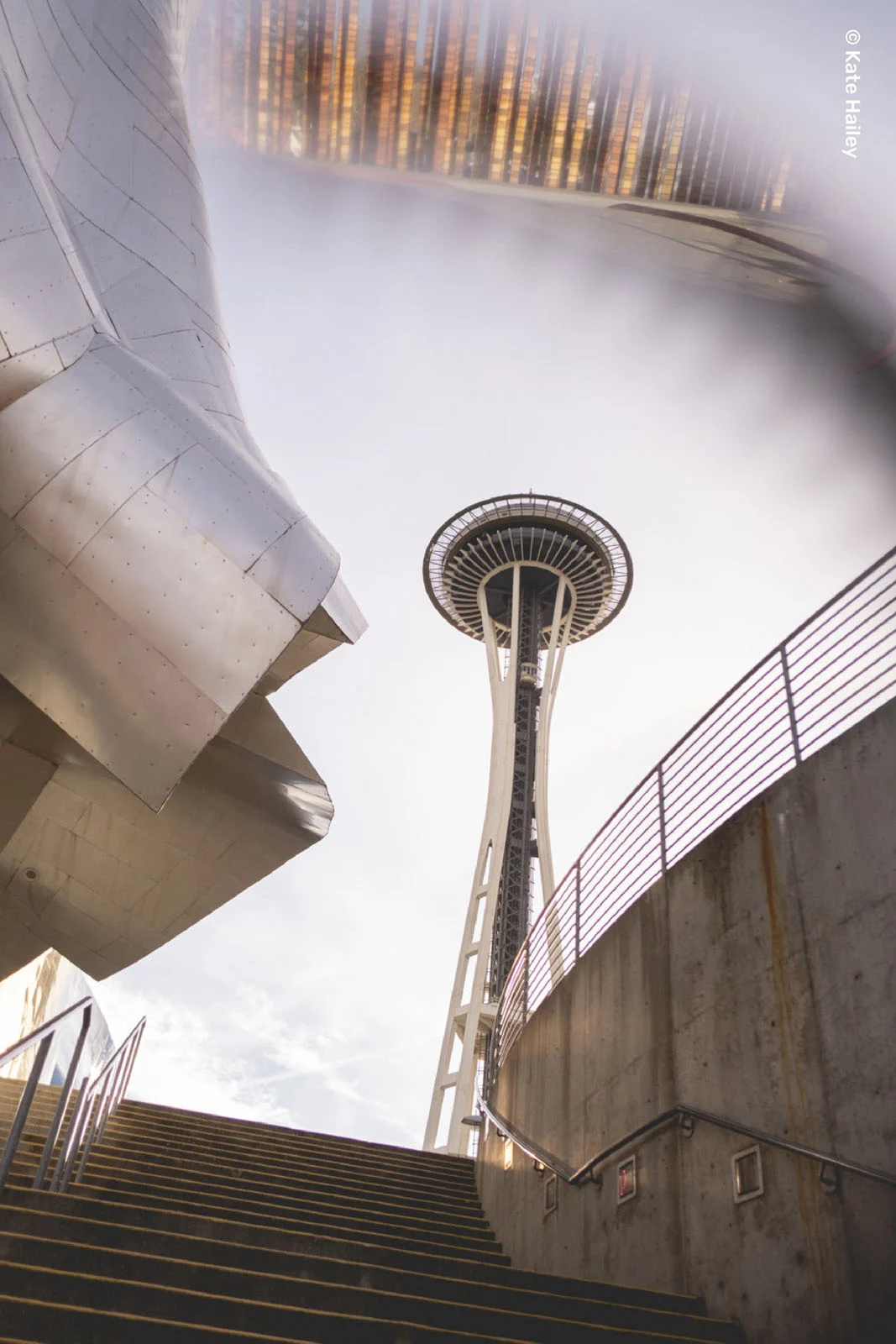 Lensbaby Omni Color II ve Omni Crystal II ile Çekim Sırasında Yaratıcı Efektler 30 A low-angle view of the Space Needle rising above a set of concrete stairs, with a metallic, curved structure on the left.