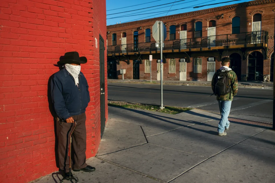 Alex Webb’in Walking Blues’u: Amerika Sokaklarında Renk, Ritim ve Rastlantı 26 Kovboy şapkası ve yüz maskesi takan yaşlı bir adam bastonuyla kırmızı tuğla duvara yaslanırken sırt çantalı genç bir adam kaldırımda uzaklaşıyor.