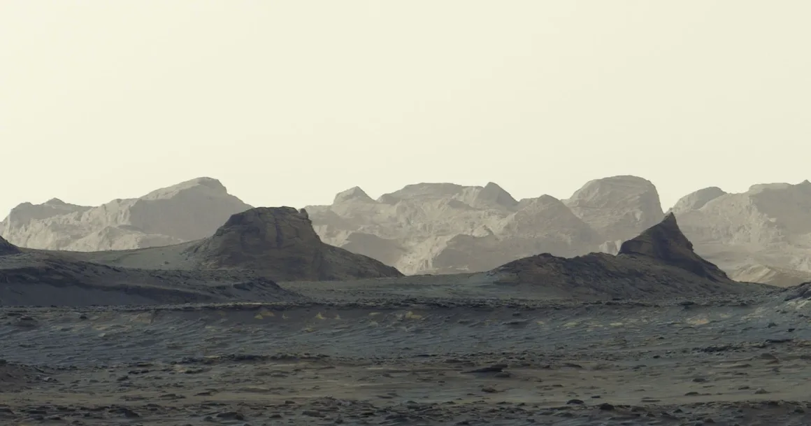Curiosity’den Bir Çarpıcı Mars Karesi Daha: Gün Doğumunda Sharp Dağı 1 Curiosity’den Bir Çarpıcı Mars Karesi Daha: Gün Doğumunda Sharp Dağı
Soluk bir gökyüzünün altında, ön planda koyu ve engebeli tepelerin, uzakta ise katmanlı dağ sıralarının görüldüğü ıssız, kayalık bir manzara.