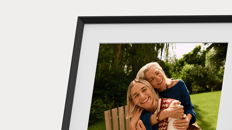 Amazon Alexa Photo Frame Tanıtıldı: Yapay Zekâ Fotoğrafları Sizin İçin Seçiyor 19 Dijital fotoğraf çerçevesinde güneşli ve yeşil bir bahçede gri saçlı yaşlı bir kadınla sarışın genç bir kadının birbirine sarıldığı görüntü yer alıyor.