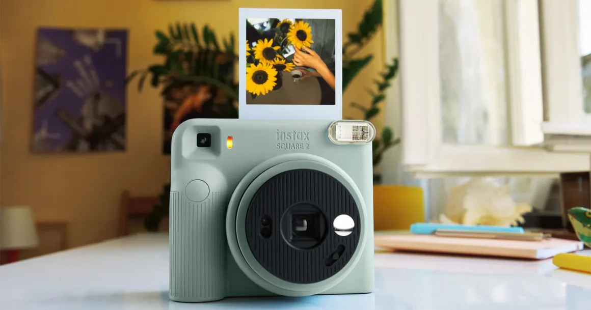Fujifilm Instax Square 2: Yeni Tasarım, Yeni Mood Filtreleri 19 Açık yeşil Instax Square 2 anlık fotoğraf makinesi beyaz bir masa üzerinde duruyor; üzerinde ayçiçeklerini gösteren geliştirilmiş kare bir fotoğraf bulunuyor.