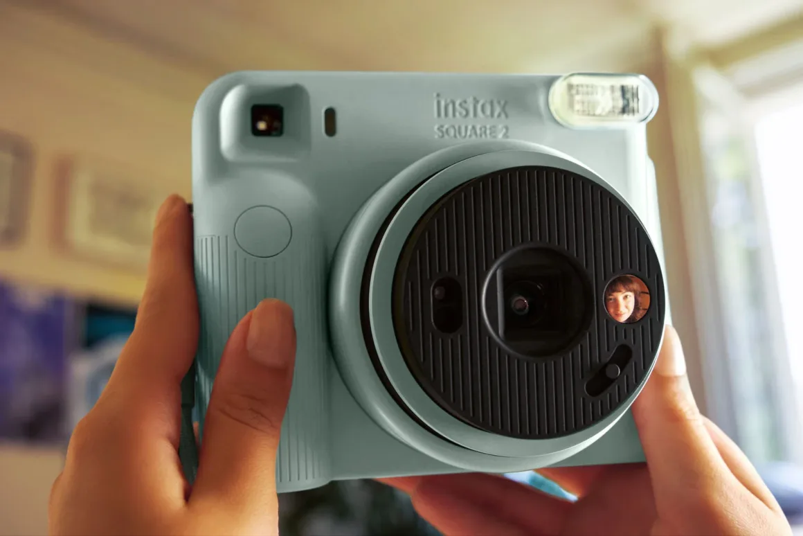 Fujifilm Instax Square 2: Yeni Tasarım, Yeni Mood Filtreleri 21 Bir kişi açık mavi Instax Square 2 fotoğraf makinesini tutuyor; objektif çevresindeki küçük dairesel aynada bir kadının yüzünün yansıması görülüyor.