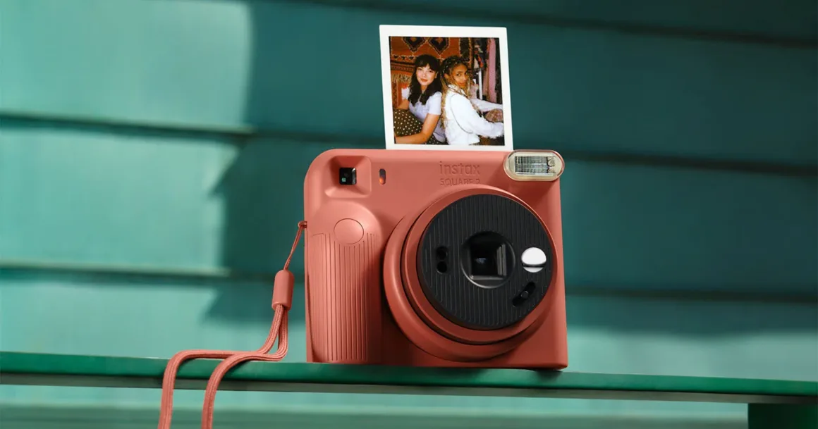 Fujifilm Instax Square 2: Yeni Tasarım, Yeni Mood Filtreleri 1 Fujifilm Instax Square 2: Yeni Tasarım, Yeni Mood Filtreleri
Terracotta renkli Instax Square 2 anlık fotoğraf makinesi, yeşil bir yüzey üzerinde duruyor; objektifin üzerinde iki kişinin yer aldığı kare bir fotoğraf görülüyor.