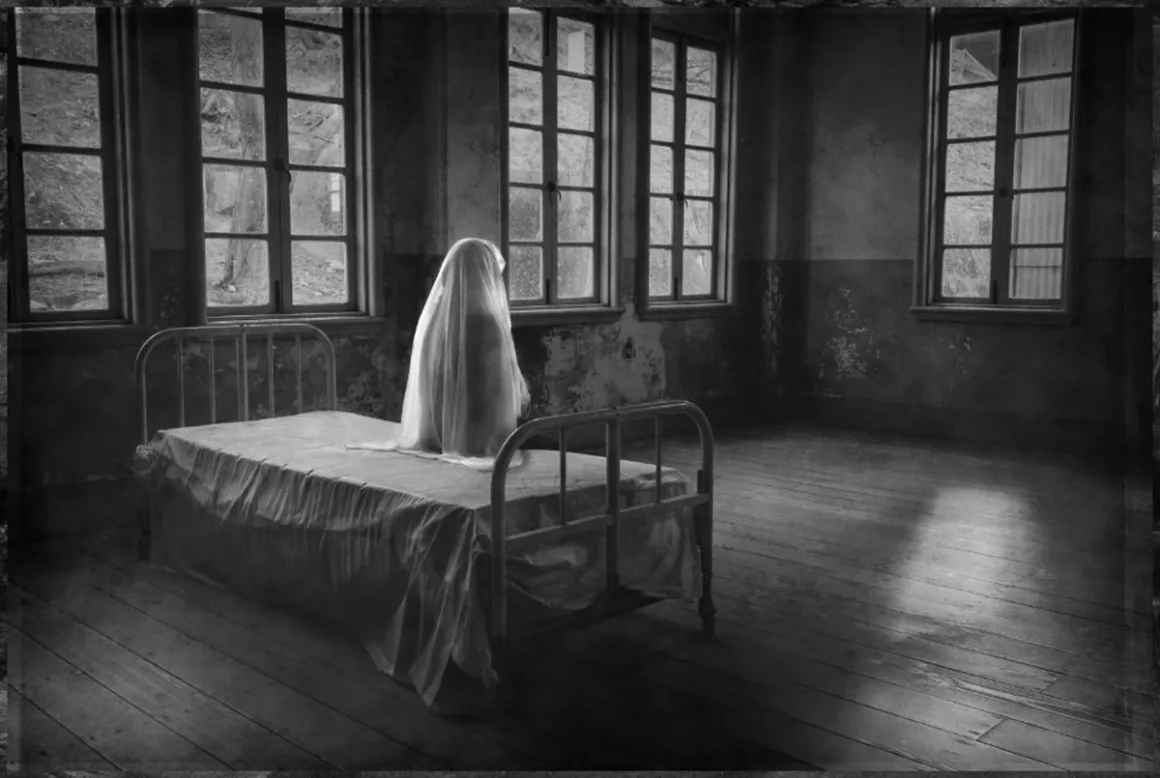 74. Nikkor Photo Contest Kazananları Açıklandı 36 Beyaz çarşafa sarılmış bir figür, büyük pencerelere sahip loş ve boş bir odada metal çerçeveli yatağın üzerinde oturuyor.