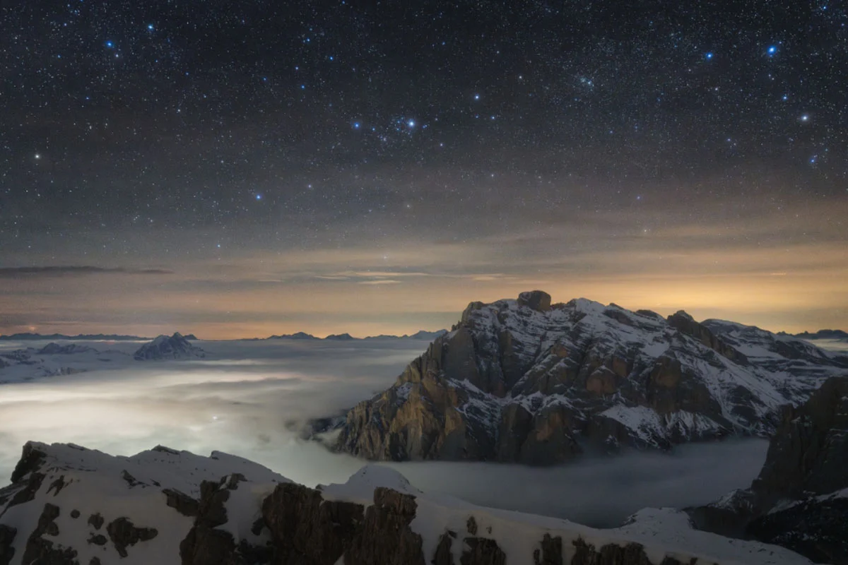 74. Nikkor Photo Contest Kazananları Açıklandı 42 A snow-covered mountain peak rises above a thick layer of clouds under a vast, star-filled night sky.