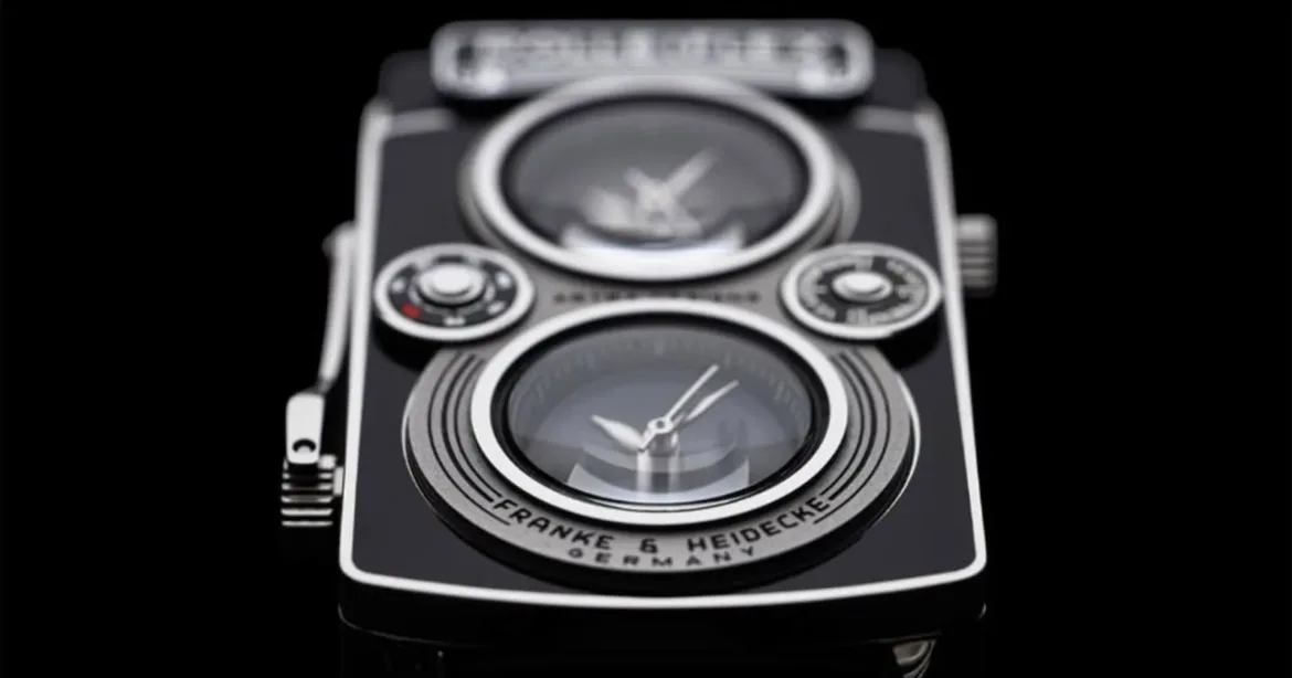 A close-up of a black and silver watch designed to resemble a vintage twin-lens reflex camera, featuring two circular clock faces and the text "FRANKE & HEIDECKE GERMANY" on the lower lens area.