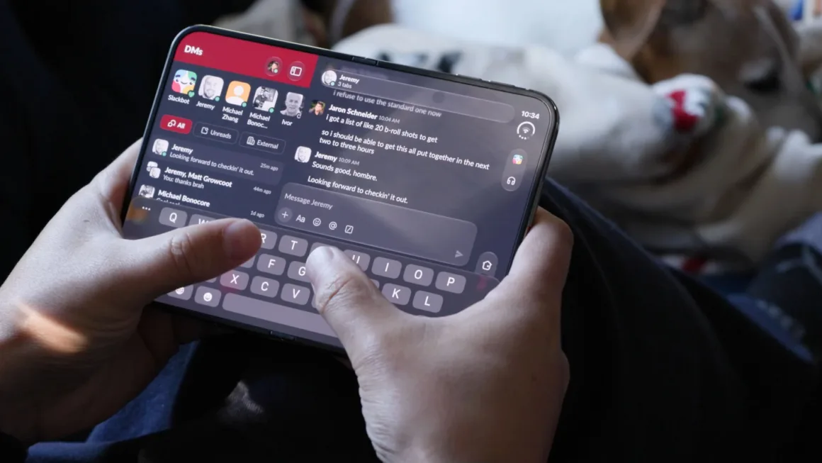 iPhone Duo İncelemesi: Etkileyici Tasarım, Kaçınılmaz Tavizler 23 Bir kişi, bölünmüş ekran mesajlaşma arayüzü ve ekran klavyesi gösteren katlanabilir akıllı telefonu tutuyor.