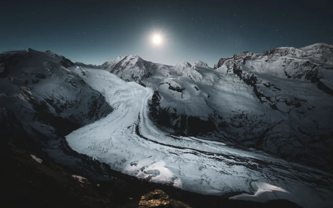 74. Nikkor Photo Contest Kazananları Açıklandı 30 Parlak Ay, yıldızlarla dolu gece gökyüzü altında koyu ve engebeli dağ zirveleri arasındaki geniş karla kaplı buzulun üzerinde parlıyor.