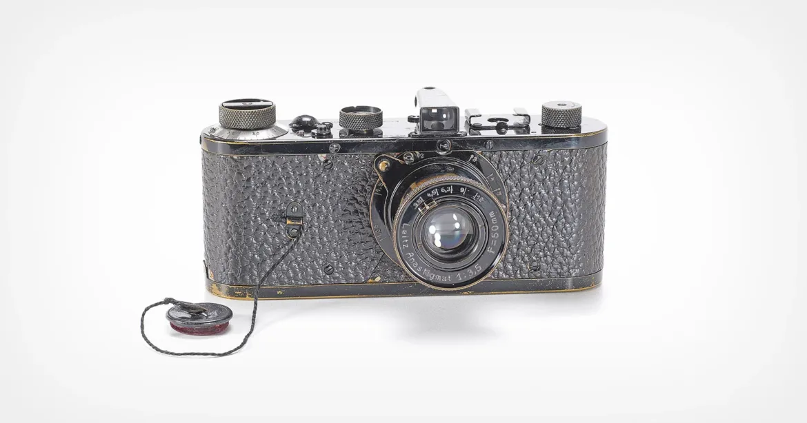 A vintage black film camera with a textured body and a lens labeled "Leitz Anastigmat 1:3,5 F=50mm," featuring a lens cap attached by a string.